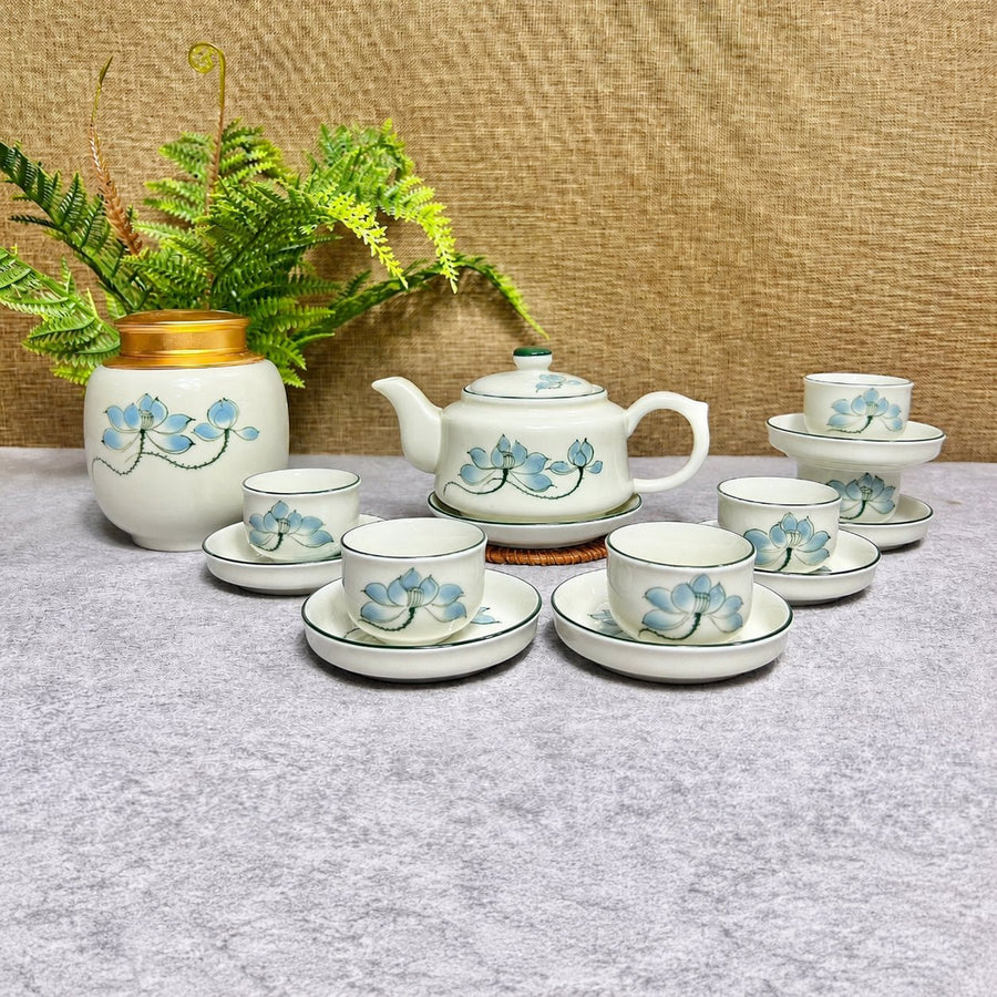 Bộ Trà Vẽ Sen nền trắng họa tiết sen xanh, gồm ấm quai bên, chén, đĩa tròn và hũ trà nắp vàng.