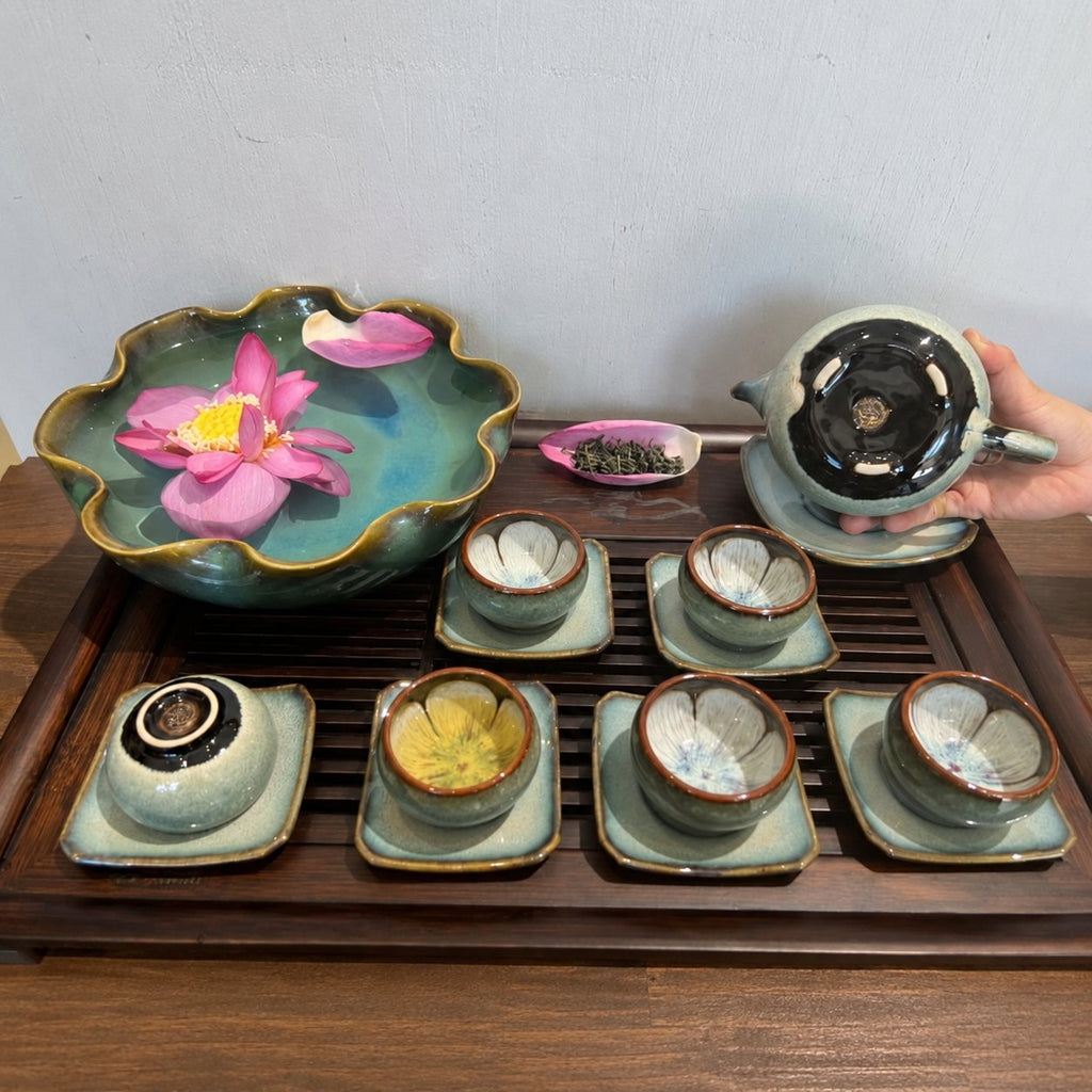 Bộ Trà Men Thỏ Ngọc với chén đặt trên đĩa vuông; một bàn tay nghiêng ấm để lộ mặt đáy.